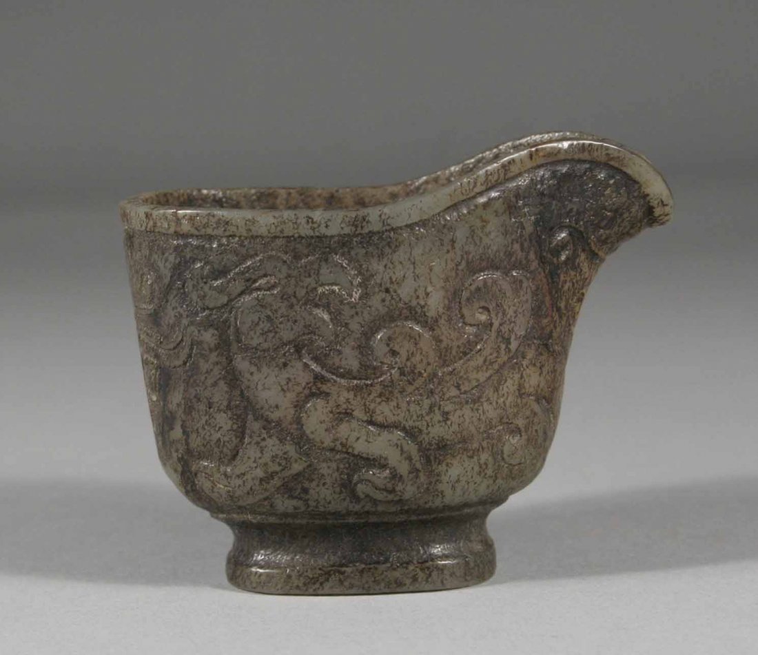 An antique Chinese altered jade libation cup of arc: An antique Chinese altered jade libation cup of archaistic form with spout and raised over a plain foot, carved in relief with a pair of stylized mythical beasts, 2.5''.