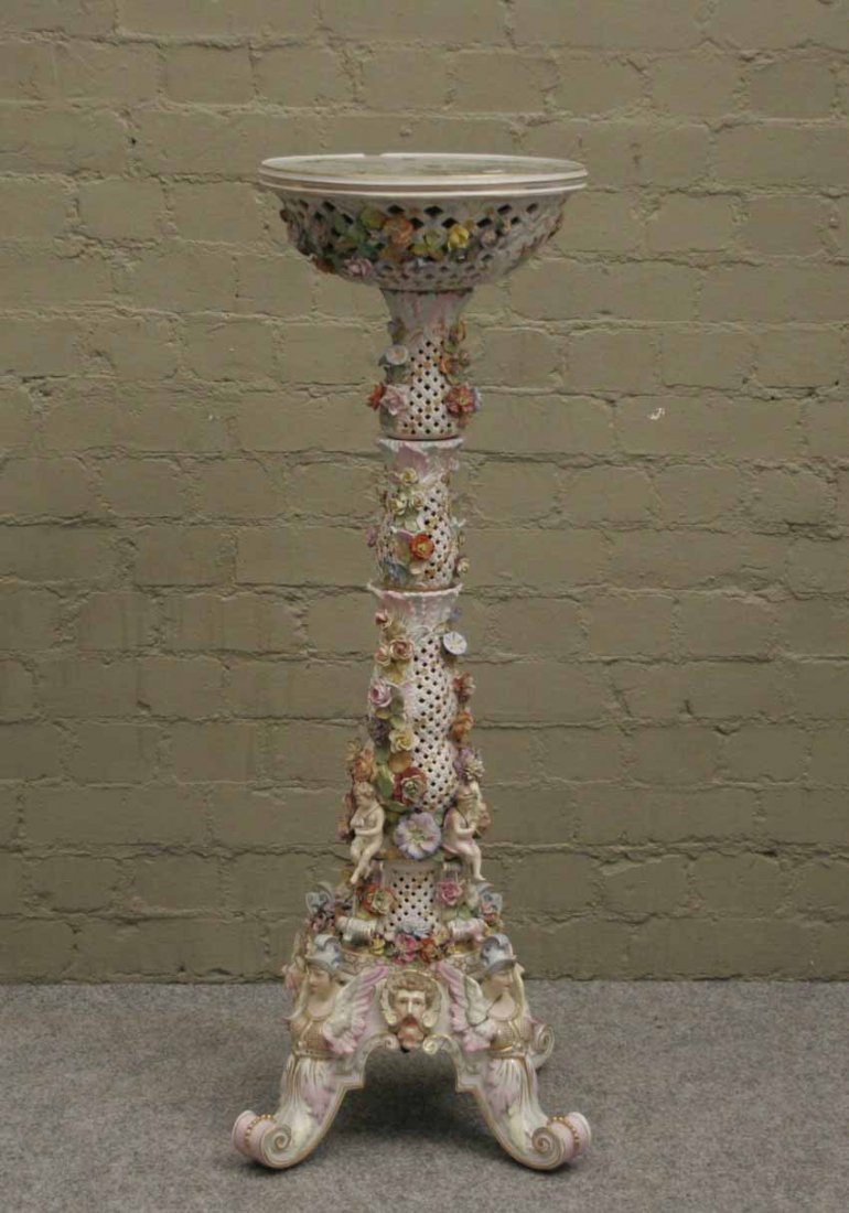 A Meissen style torchere raised on scrolling suppo: A Meissen style torchere raised on scrolling supports with pierced trellis work, ornamented with putti and applied flowers, 43''