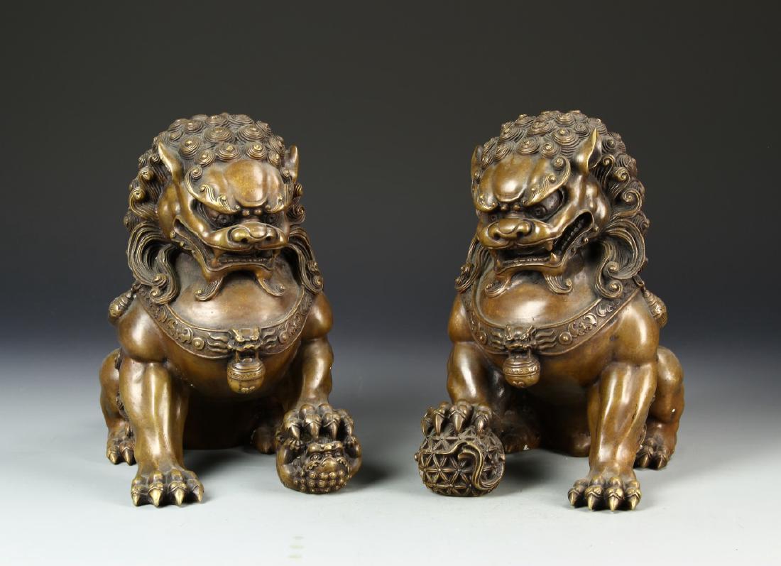 Pair of Chinese Bronze Foo Dogs: China, ROC, a pair of bronze foo dogs, intricate and expressive carving of two complimentary statues, with open mouths, teeth showing, one large paw raised upon a ball, details in mane, fur and tails.