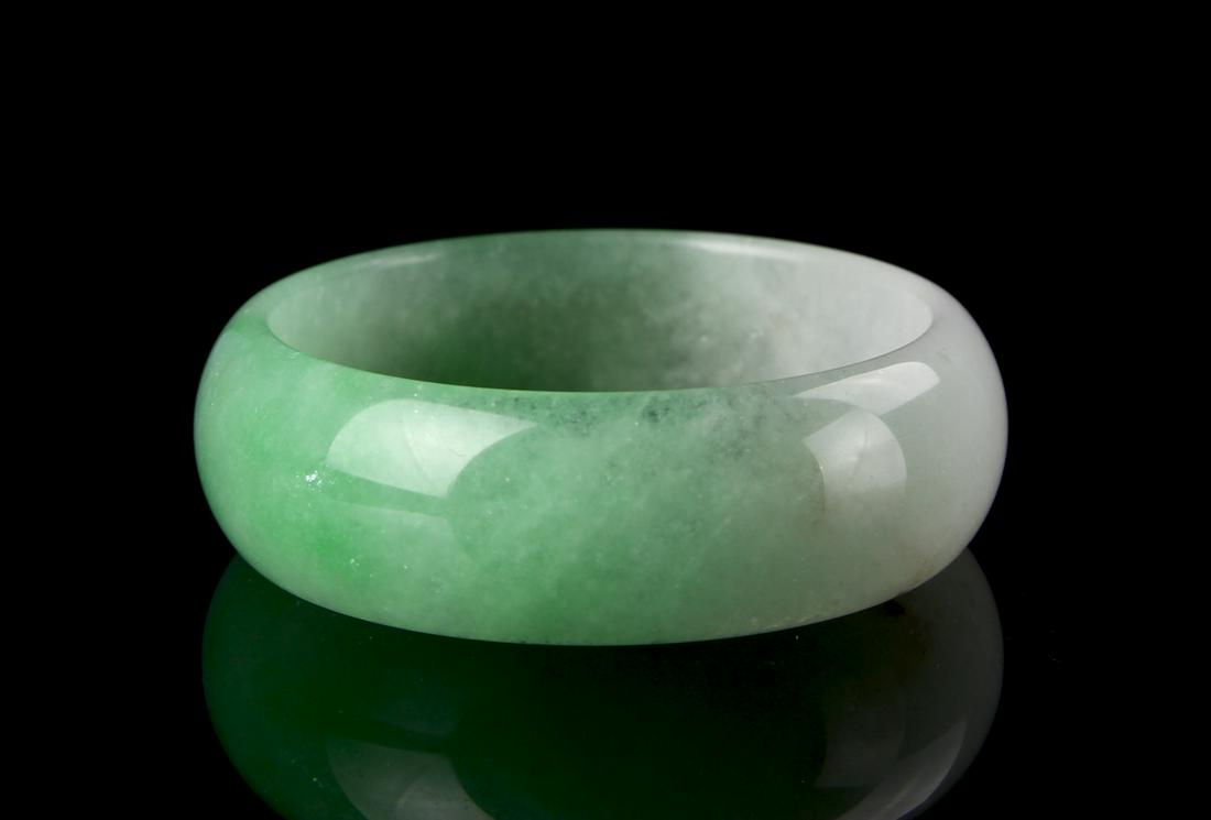Chinese Jadeite Bangle: China, jadeite bangle, thick rounded edges, mottle green throughout with white hue splashes, smooth surface, high sheen. Diameter 2 7/8 in.