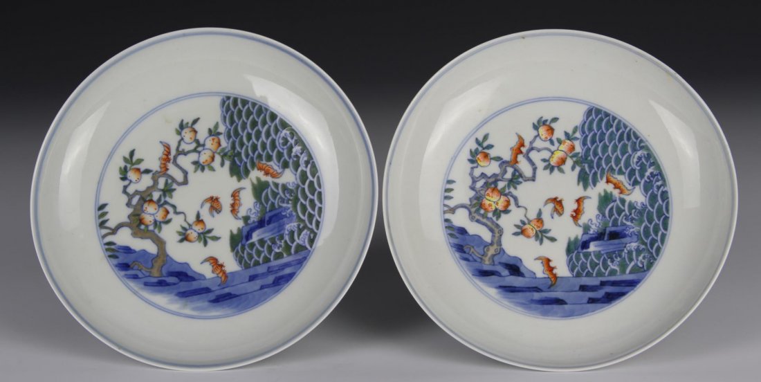Pair of Doucai Dishes: China, Qing period, painted with a fruit bearing peach tree emerging from rocky cliff with bats hovering over crested waves below, six characters, Yongzheng mark. Diameter 6 1/4 in. Provenance: Estate