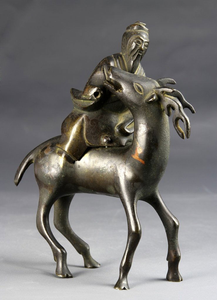 Chinese Bronze Incense Burner: China, bronze incense burner in the form of a robed, elder figure perched on the back of a deer with antlers. Height 5 in., Width 7 in.