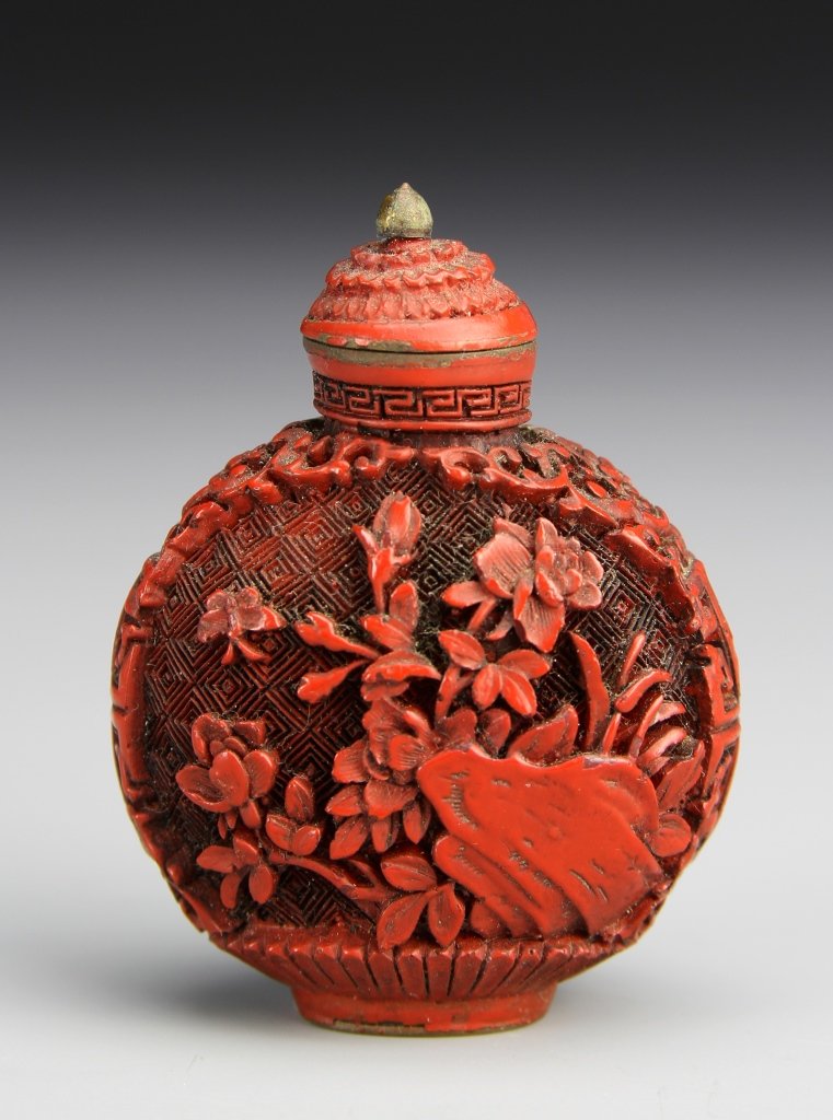 Chinese Cinnabar Snuff Bottle: China, 19th C., Cinnabar snuff bottle in a flattened ovoid form, densely decorated with carved relief on both sides of flowers, plants and insects, with patterned design in the ground, stopper with gi