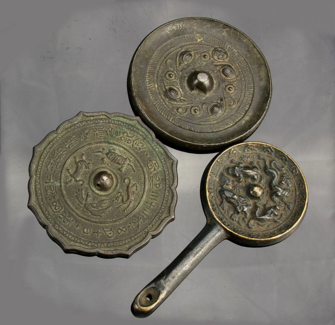 Three Chinese Antique Mirrors: China, three antique mirrors; one with a scalloped edge; one with a rounded edge, and one handled with a rounded edge, each decorated with auspicious symbols. Diameter of largest, 3 in.