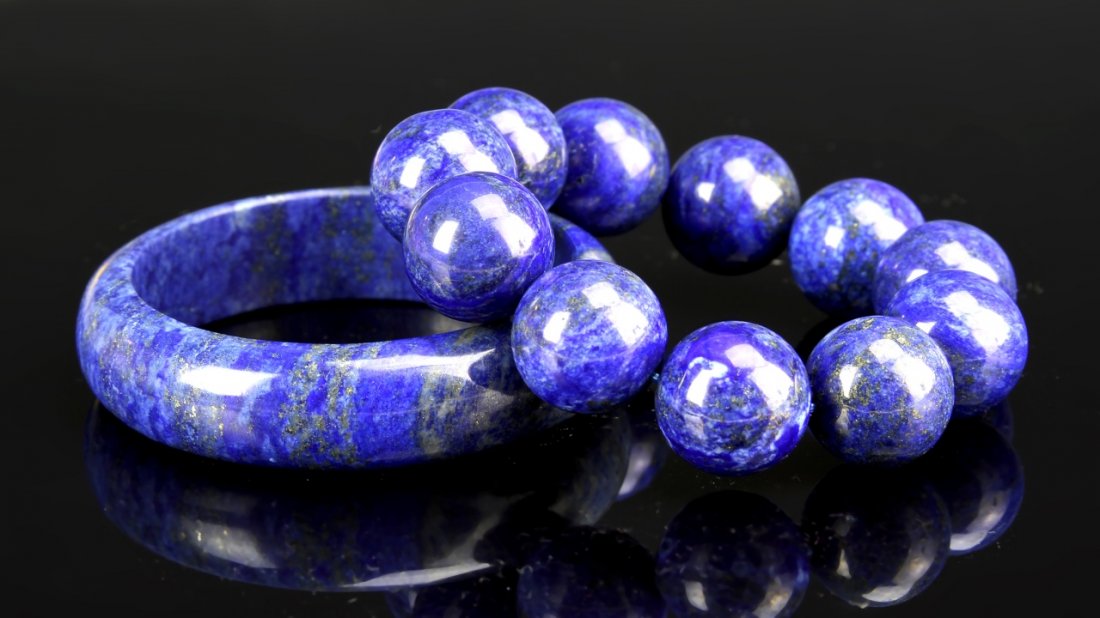 Chinese Lapis Lazuli Bracelets: China, two smoothly carved lapis lazuli bracelets of dark blue with gray and white color variations throughout, one of the bracelets is a smooth bangle and the other a string of similar sized beads. B