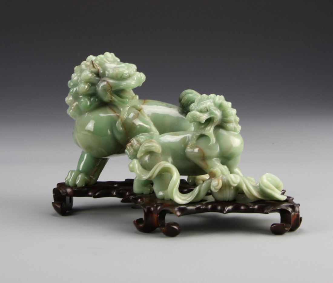 Chinese Jade Foo Dogs: China, carved jade foo dogs with wooden stand, made of light green stone with several brown veins, one larger dog with head to the side and front paw on the rump of a second smaller dog. Height 7 1/4 