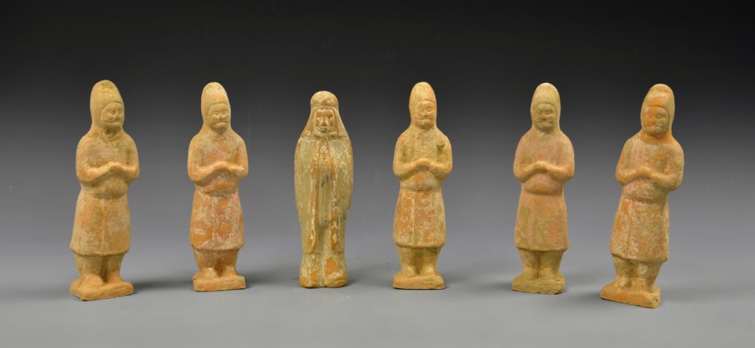 Six Chinese Pottery Figures: China, Han Dynasty, six standing pottery figures with fading umber coating, five identical male forms in plain hooded robes, one figure in more elaborate flowing clothes with blue accents. Height 9 in
