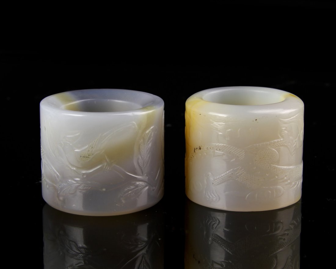 Two Chinese Carved Thumb Rings: China, 19th C., two carved thumb rings of light brown stone, one with white and dark gray striations, carved with plant and dragon motifs. Largest Height 1 1/8 in.