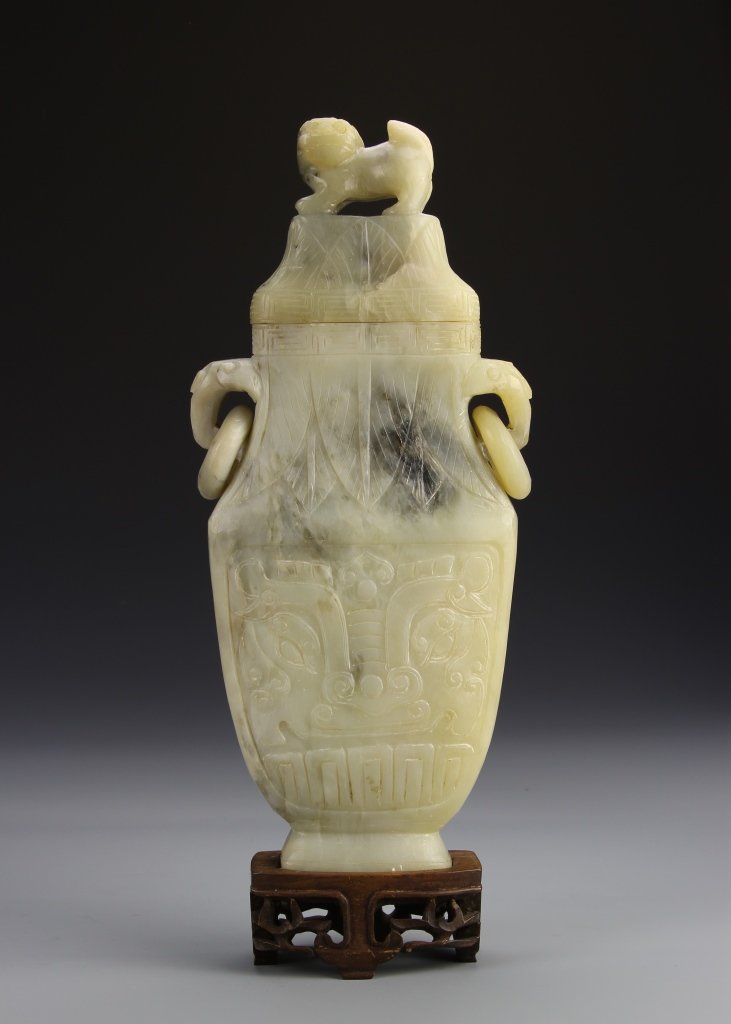 Chinese Jade Vase: China, jade vase on wood stand, high shoulder, narrow neck, with intricately carved attached looped ears, hanging hoops attached to ears, mythical figure seated atop. Height 11 1/2 in.