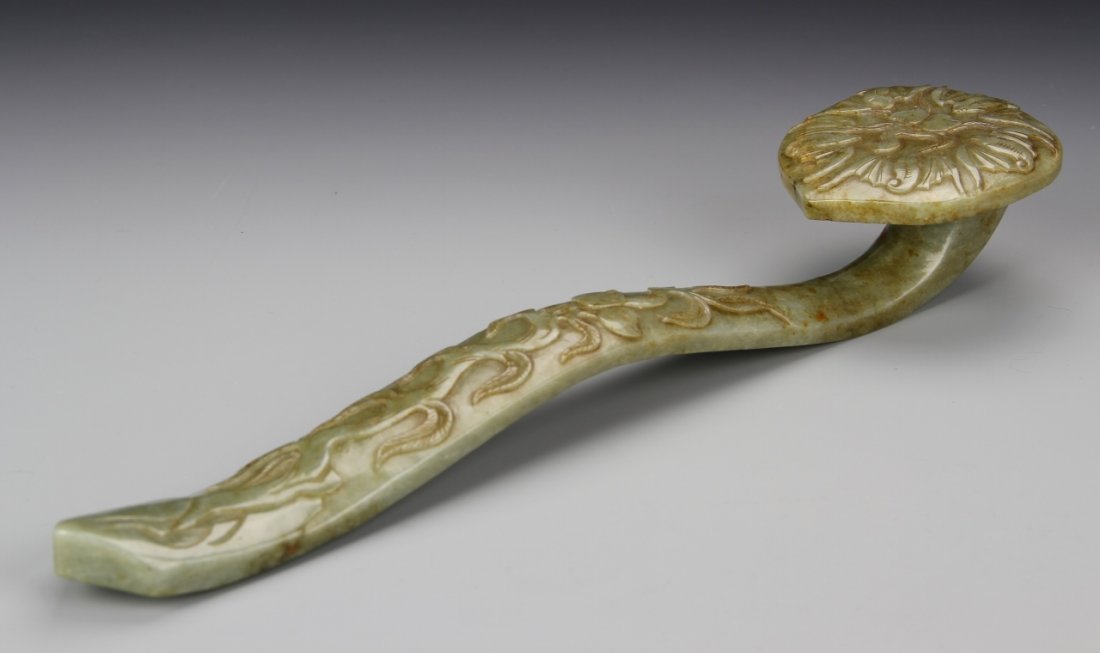 Chinese Carved Jade Ruyi Scepter: China, 19th C., carved jade Ruyi scepter, with floral motifs on the surface, in a light green hue, with striations in the stone, and calligraphy marks on back. Length 12 3/4 in.