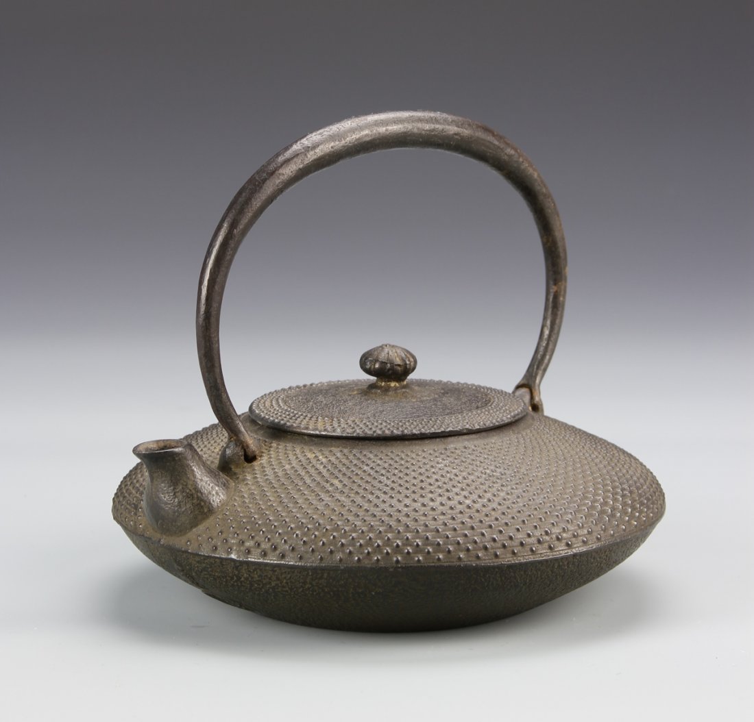 Japanese Iron Teapot: Japan, antique iron teapot with cover, flattened form with large handle ring, upper body patterned with small studs, rough surface on bottom and base, mark on side. Height 6 1/4 in., Diameter 7 in.