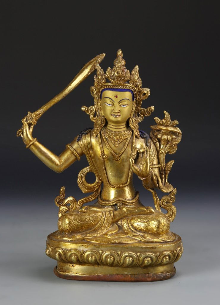 Chinese Tibetan Gilt Bronze Buddha: China, Tibet, gilt bronze Buddha, in a seated position, holding a sword, with flowing robes, face and head brightly colored with hues of blue and red, on a lotus base. Height 12 in.