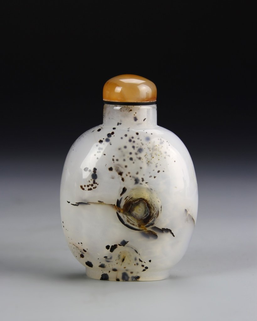 Chinese Agate Snuff Bottle: China, agate snuff bottle, baluster body in white stone with black and brown variations in organic patterns throughout, with an orange colored stopper. Height 3 in.