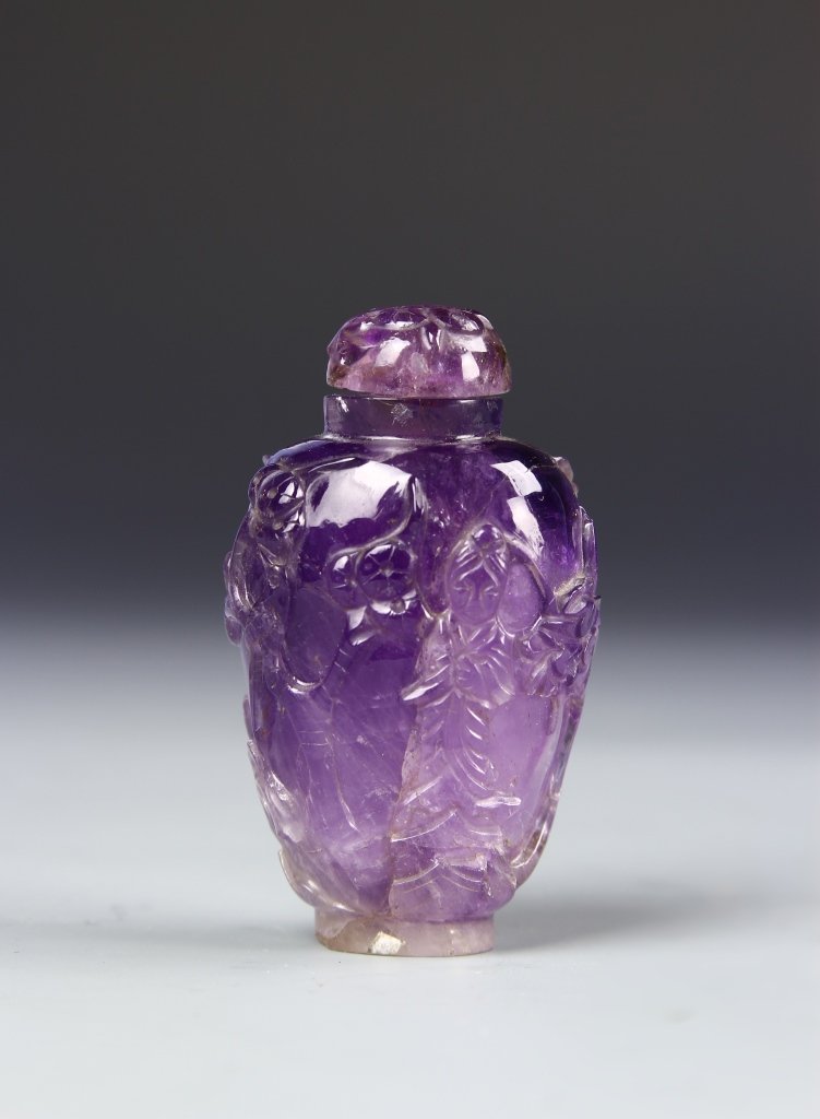 Chinese Amethyst Snuff Bottle: China, 19th Century, carved amethyst snuff bottle with roughly carved faces and figures adorning, and a gradient, deep to light purple hue from cap to base. Height 2 1/2 in.