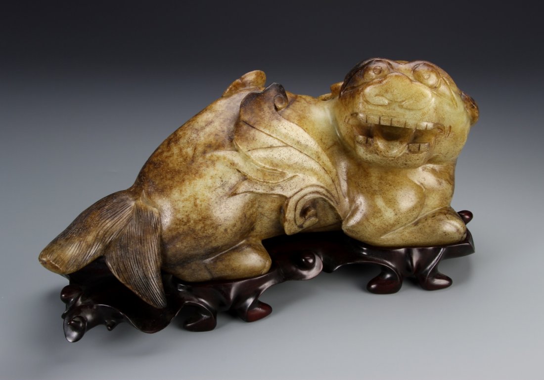 Chinese Jade Mythical Animal: China, expertly carved jade figure of a mythical animal, in a reclining position, with a ferocious expression on the face, and a fish tail with fins, with a carved wooden base. Height 15 in., Width 6 