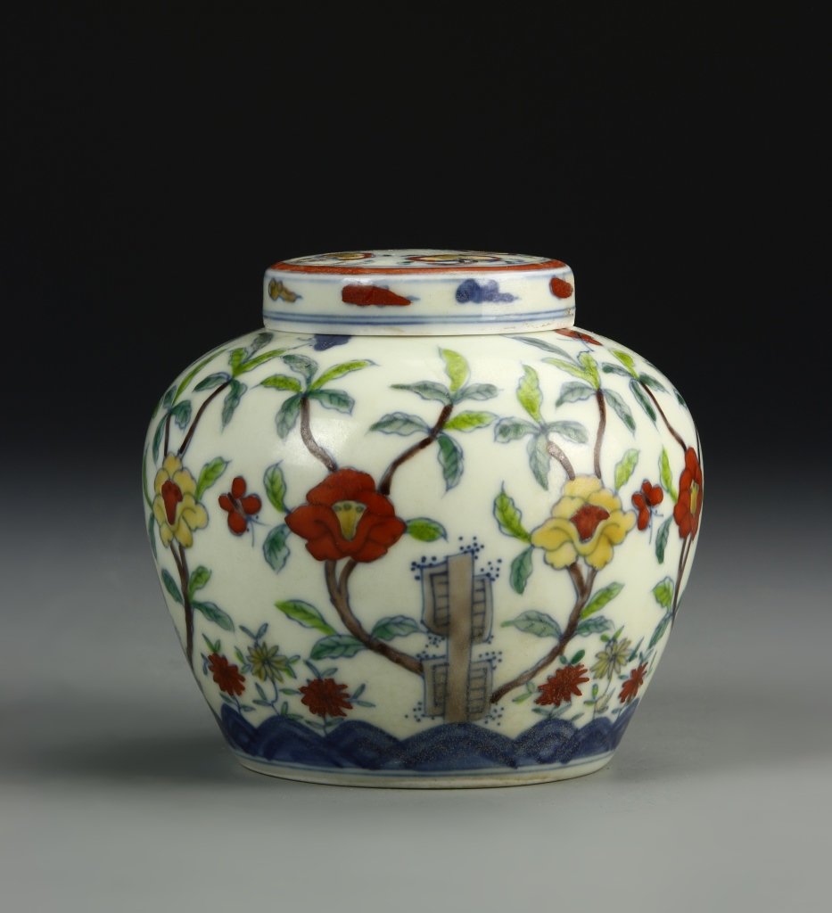Dou-T'sai Jar and Cover: The globular body rising to a short neck, painted in bright doucai enamels with camellia and red blooms growing from blue enameled ornamental rockwork, the flat circular cover decorated with ruyi head