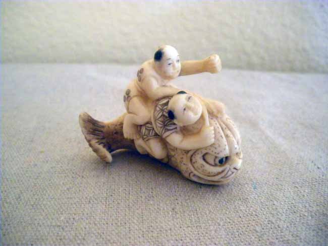 Chinese Carved Ivory Netsuke 2 Male Figures atop F: A Chinese carved ivory netsuke depicting two male figures atop a Fish.