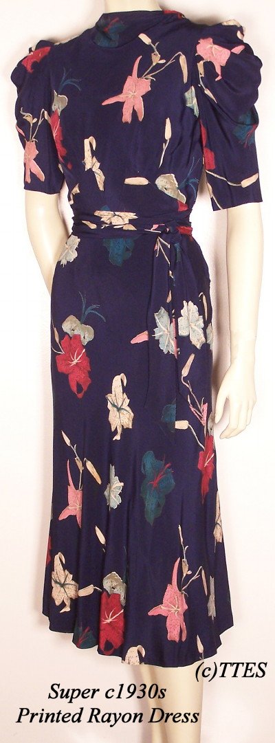 Super c1930's Lady's Printed Rayon Dress: A colorful lily print on deep navy blue gabardine, with pleated shoulders, a bias cut skirt, a matching belt sash, and neck streamers at the back. Snap closures at the back and side. A 32" bust, 25" w