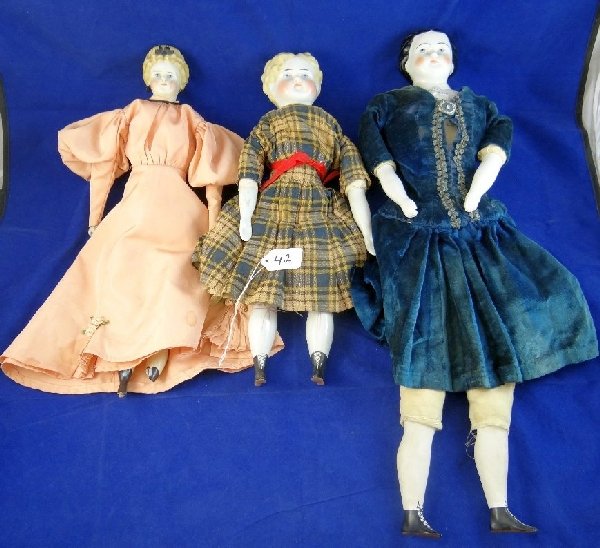 Lot of (3) Antique Porcelain Dolls: Great Collectors Pieces. Their faces have nice detail. They have beautiful dresses. All the dolls are in great condition except one has a broken foot. Measure approx. 16" x 21"