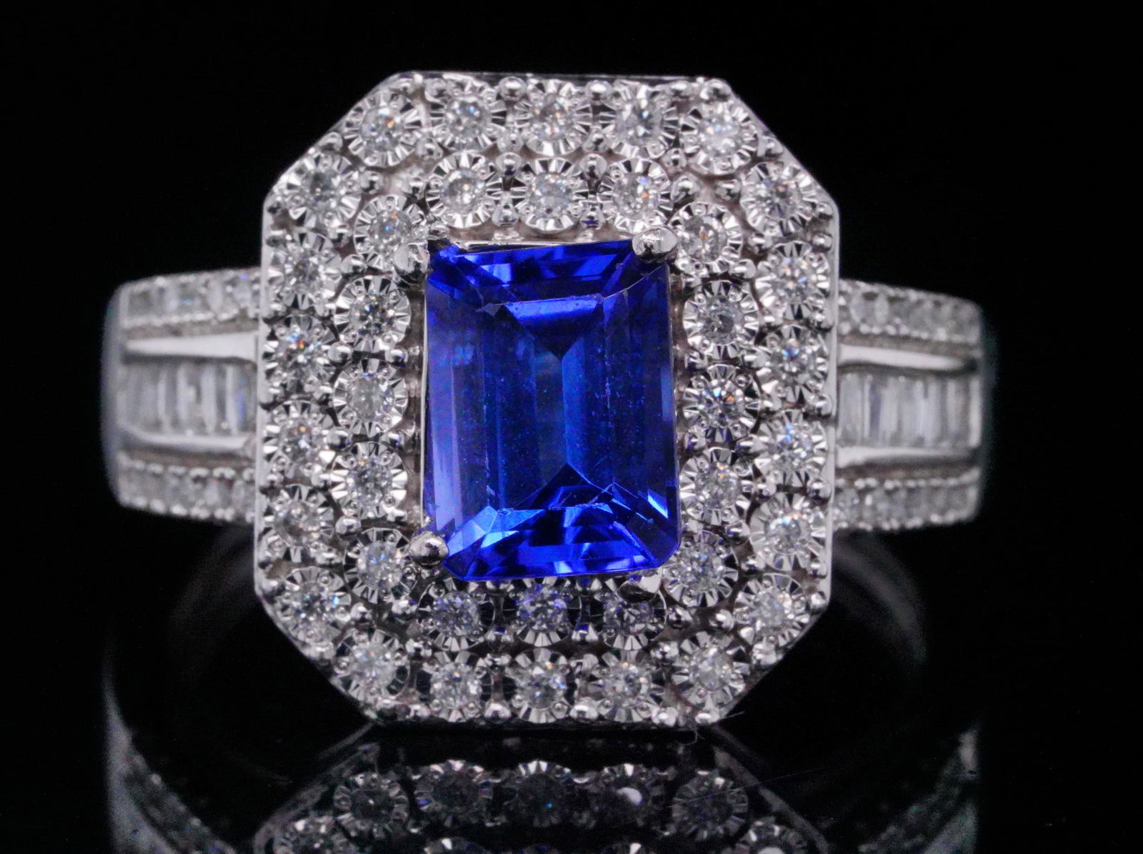 1.50ct Tanzanite, 0.50ctw Diamond and 14K Ring: 1.50ct Tanzanite, 0.50ctw Diamond and 14K White Gold Ring - A striking ring showcasing a 1.50 carat emerald cut tanzanite of vivid bluish violet hue, framed by a halo of round cut diamonds that enhanc