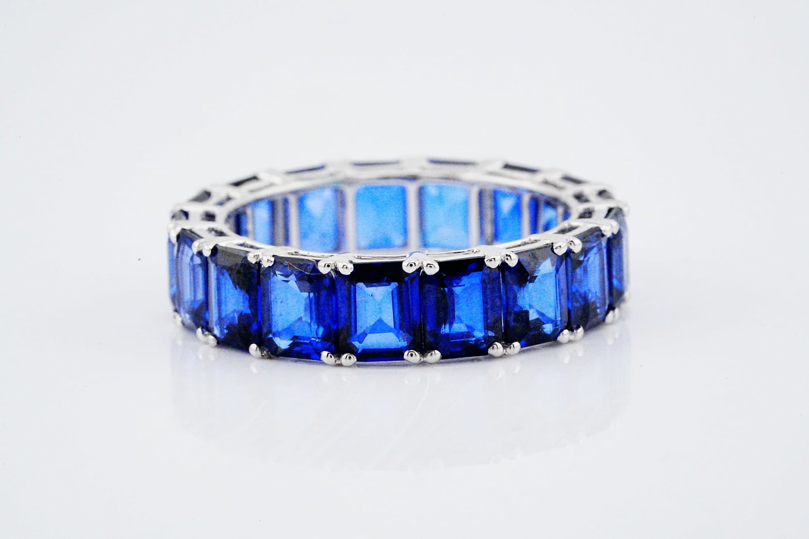 9.10ctw Blue Sapphire and 18K 5.4mm Wide Eternity Band: 9.10ctw Blue Sapphire and 18K White Gold 5.4mm Wide Eternity Band - THIS ITEM WILL COME WITH A $5,000 INSURANCE VALUATION REPORT. Elegantly crafted in polished 18K white gold, this refined eternity ba