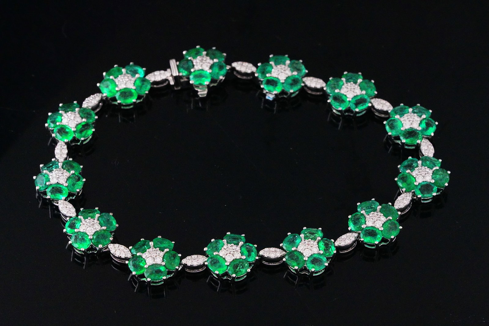 11.15ctw Emerald, 1.25ctw Diamond and 18K Bracelet: 11.15ctw Emerald, 1.25ctw SI1-SI2/G-H Diamond and 18K White Gold 7.25" Floral Line Bracelet - THIS ITEM WILL COME WITH A $25,000 INSURANCE VALUATION REPORT. This elegant floral line bracelet features 