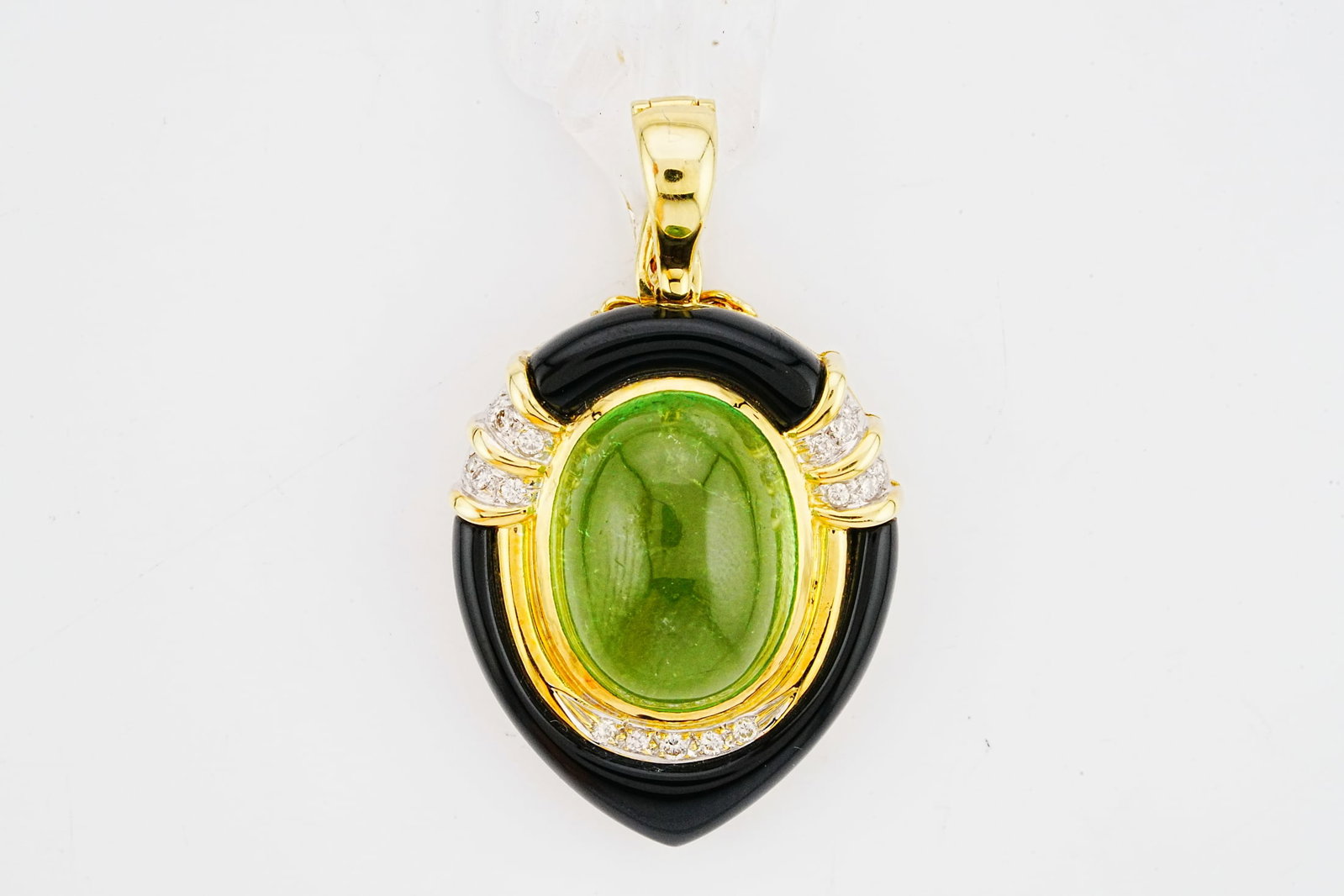 15.00ct Tourmaline, 0.25ctw Diamond, Onyx, 14K Pendant: 15.00ct Green Tourmaline, 0.25ctw Diamond, Onyx and 14K Yellow Gold 1.75" Pendant - This striking pendant features a vibrant green tourmaline cabochon weighing approximately 15.00 carats. The oval cab