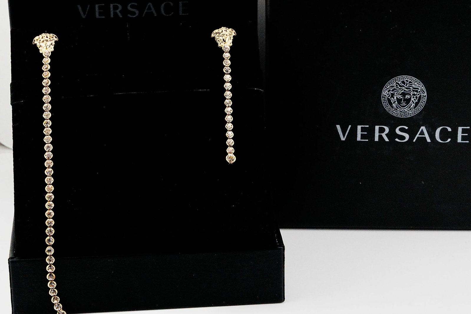 Versace Strass Crystal Asymmetrical Medusa Earrings: Versace Strass Crystal Gold Tone Asymmetrical Medusa Dangle Earrings Never Worn W/Original Box - A striking and unmistakably glamorous pair of Versace asymmetrical dangle earrings featuring the house'