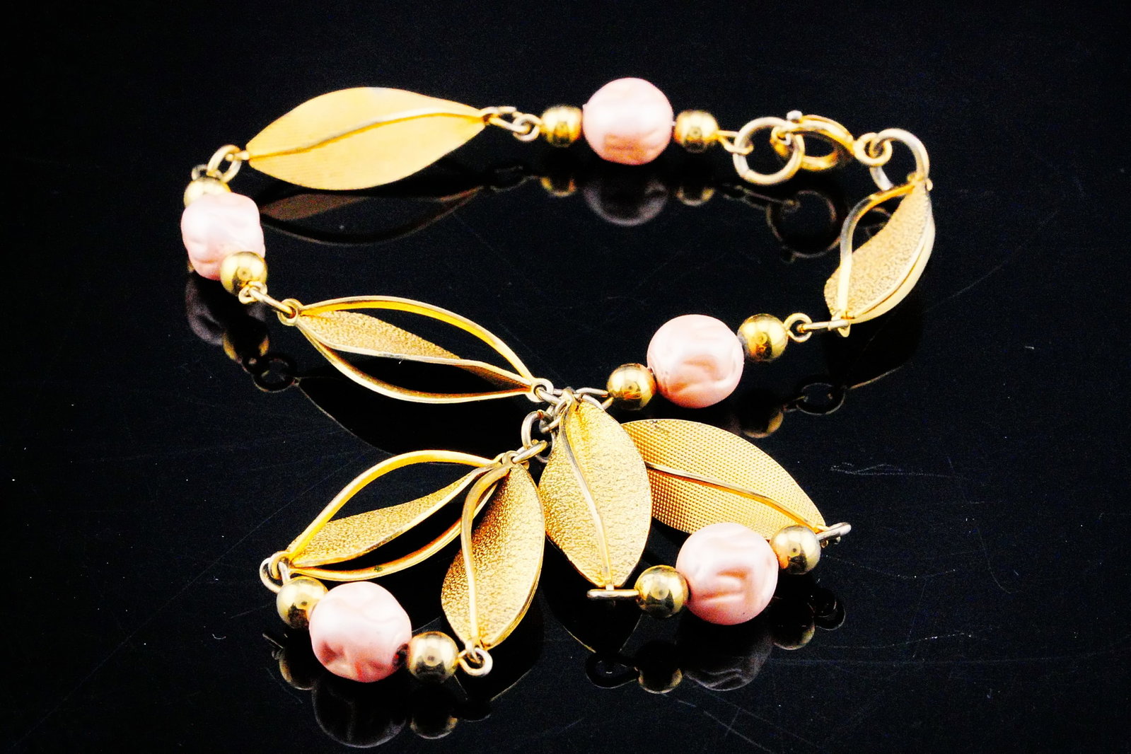 German Pink Faux Pearl Gold Tone Textured Leaf Bracelet: German Pink Faux Pearl Gold Tone Textured Leaf Dangle Bracelet - A charming and feminine fashion bracelet featuring lustrous pink faux pearls accented by richly textured gold tone leaf motifs in an