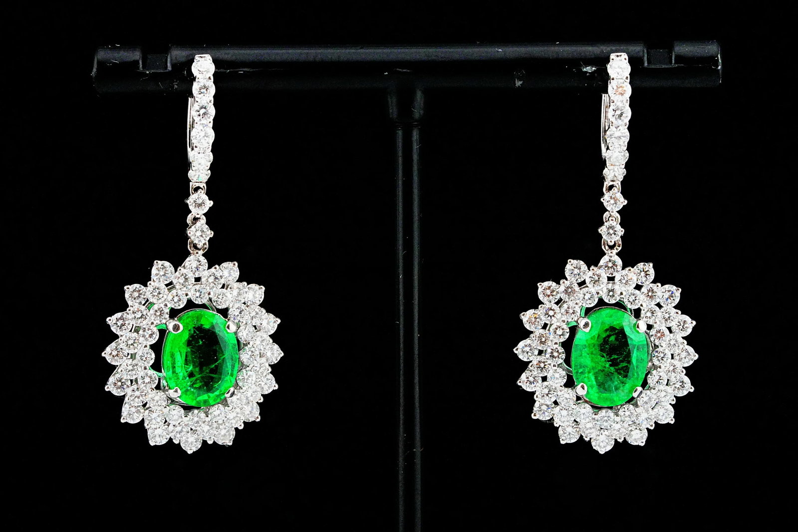 3.90ctw Diamond, 3.20ctw Emerald and 18K Earrings: 3.90ctw VS1-SI1/G-H Diamond, 3.20ctw Emerald and 18K White Gold 1.25" Drop Earrings - Exquisitely crafted in 18K white gold, these elegant drop earrings are centered by a matched pair of oval-cut emer