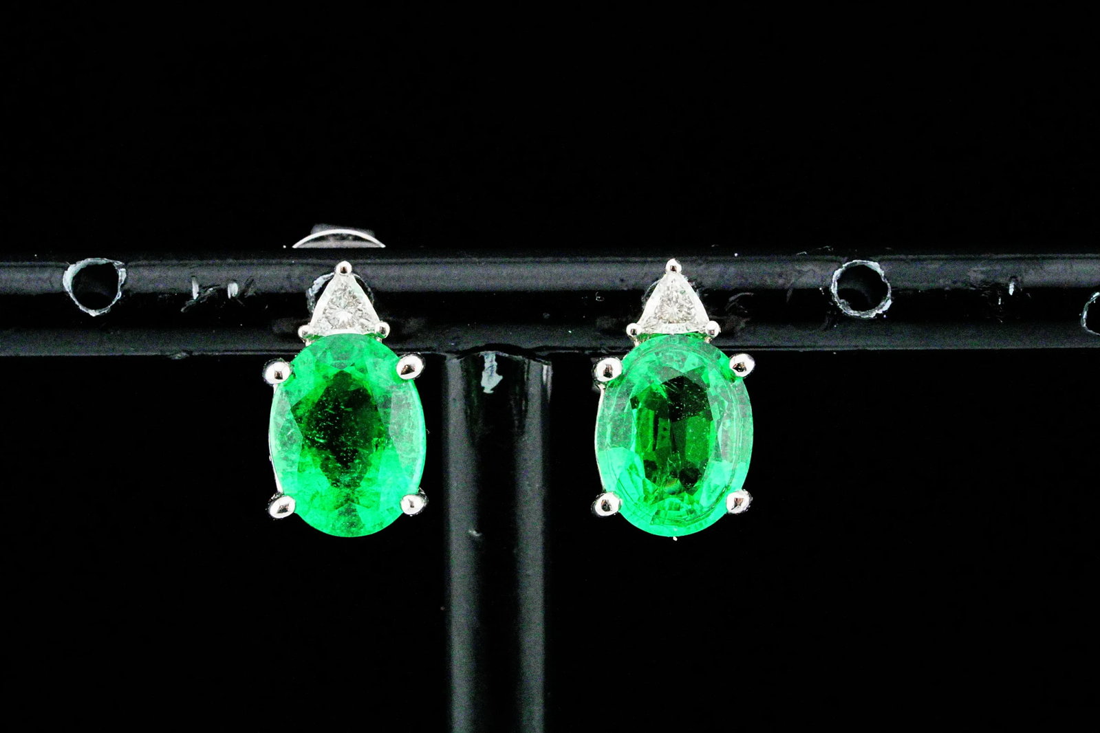 3.00ctw Emerald, 0.15ctw Diamond and 18K Earrings: 3.00ctw Emerald, 0.15ctw Diamond and 18K White Gold Stud Earrings - Expertly crafted in 18K white gold, these elegant stud earrings showcase a beautifully matched pair of oval-cut emeralds totaling ap