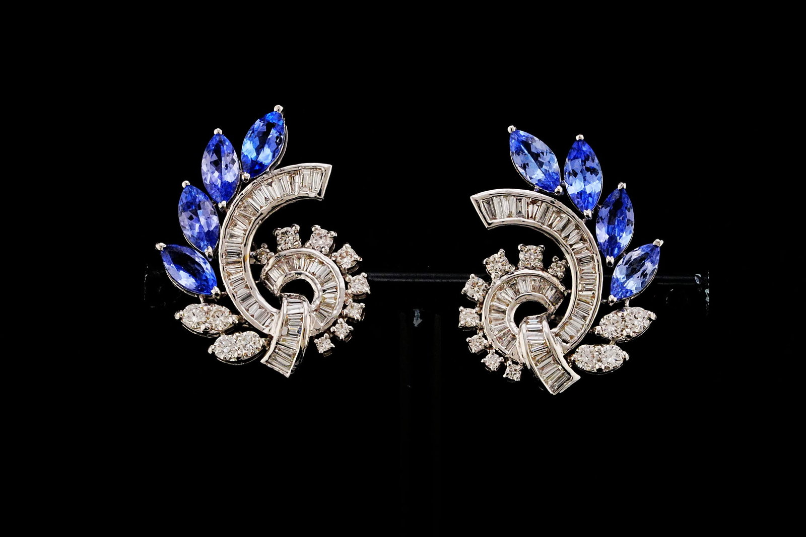 4.25ctw Tanzanite, 2.50ctw Diamond and 18K Earrings: 4.25ctw Tanzanite, 2.50ctw VS1-SI1/G-H Diamond and 18K White Gold 1.25" Cluster Swirl Earrings - THIS ITEM WILL COME WITH A $19,000 INSURANCE VALUATION REPORT. These elegant swirl earrings showcase ap