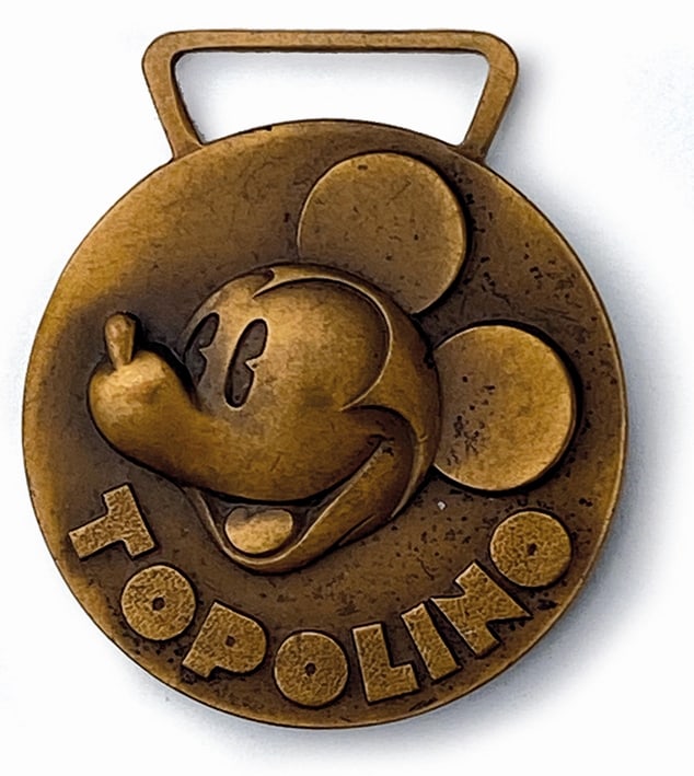 Topolino Medaglia Campionato 1938: Medaglia in vermeil, 1938. Figura alto rilievo fronte-retro. Diametro cm 3. Coniata per premiare i vincitori del campionato “Gara di Pazienza” indetto dall'Almanacco Topolino Paperino 1939. Pu