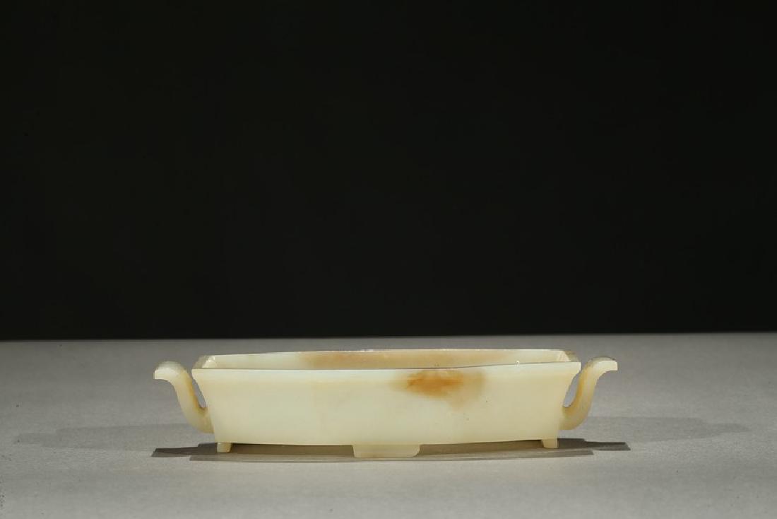 A WHITE JADE BRUSH WASHER: The shaped rectangular washer carved with two s shaped handles and supported on four stubs, the stone is of even white tone with areas of russet inclusions. Height: 1 3/16 in (3 cm) Length: 6 11/16 in