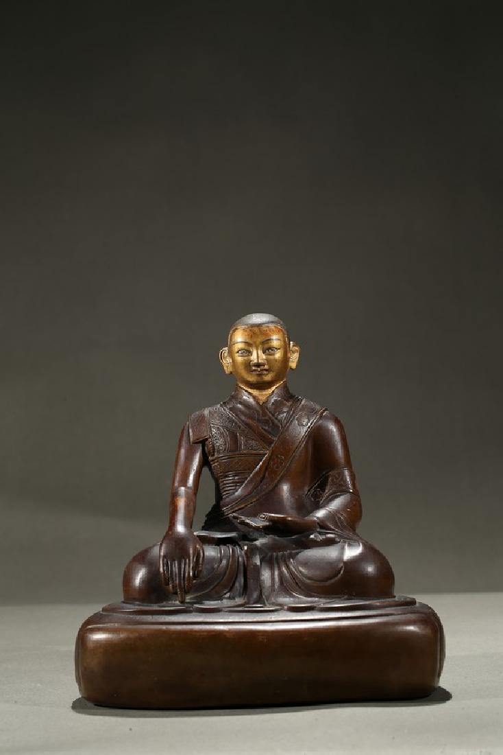 A COPPER ALLOY FIGURE OF COLD-GILDED LAMA: Depicted seated in dhyanasana on a large rounded plinth, his right hand rendered in bhumisparsa and his left in dhyanamudra, wearing robe with incised hem, face cold-gilded, the base unsealed. Qing Dy