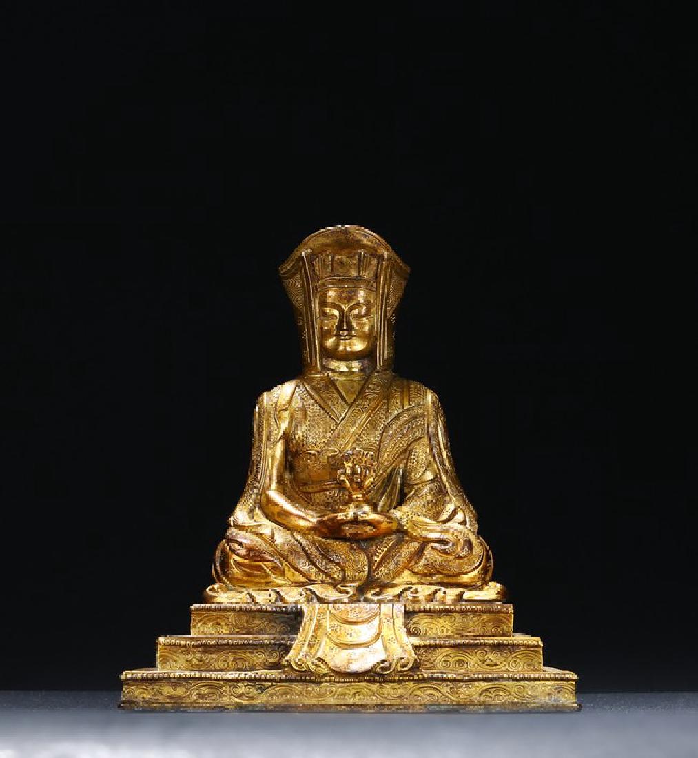 A GILT-BRONZE OF SEATED GURU: Seated on a stepped plinth, hands holding a ritual object, wearing voluminous robe decorated dense pattern, face in meditation. Qing Dynasty period. Height: 7 1/4 in (18.4 cm) Width: 6 1/2 in (16.5 cm