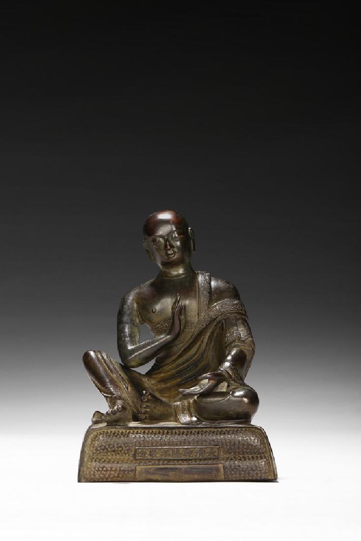 A BRONZE CAST FIGURE OF SARIPUTTA: The figure is shown seated on a plinth with inscriptions to the front and back, both hands raised in mutra, wearing a loose dhoti revealing right shoulder, the face in meditative expression. Mid Qing