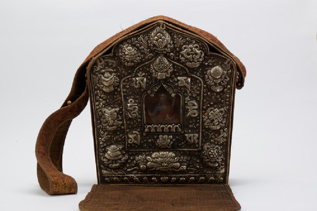 A COPPER TIBETAN TRAVELING SHRINE GAU BOX: The front of the arched box with beaded borders and elaborate repoussÃ© decoration of scrolling foliage and Buddhist precious objects above a kirtimukha mask ,all framing a central panel of conformi