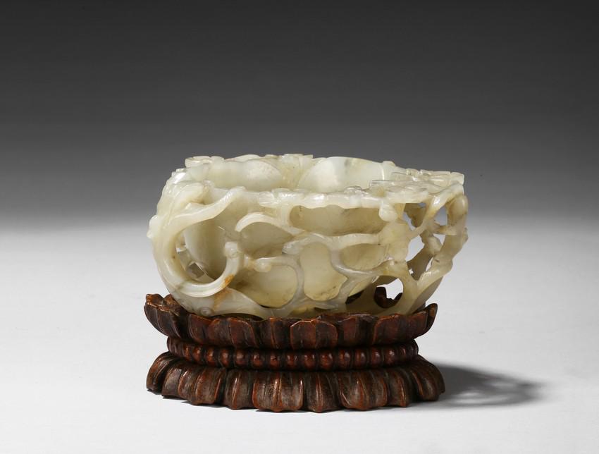 A WHITE JADE 'PLUM BLOSSOM AND CHILONG' WASHER W/ STAND: Deftly carved in the form a rounded lotus leaf, the washer is surrounded with branches of plum blossom flowers rising to the rim to one side, the other side with a climbing chilong, the stone of a gre
