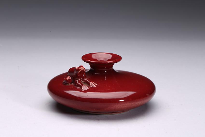 A SMALL RED GLAZE 'FROG' VASE: Of compressed globular form, the body carved with a frog in high relief, overall suffused with attractive red glaze. H: 2 1/2 in (6.3 cm) D: 5 3/4 in (14.6 cm)