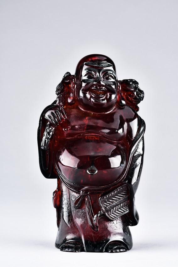 AN AMBER CARVED ARHAT FIGURE: Carved in the form of a standing arhat, with large belly exposed, the face with joyful expression. H: 7 in (17.7 cm)