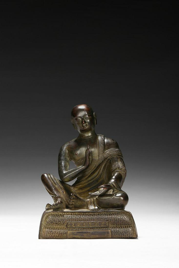 A BRONZE CAST FIGURE OF SARIPUTTA: The figure is shown seated on a plinth with inscriptions to the front and back, both hands raised in mutra, wearing a loose dhoti revealing right shoulder, the face in meditative expression. Qing Dyna