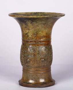 AN ARCHAIC CHINESE BRONZE RITUAL ZUN VESSEL: The central bulb cast in relief with a pair of taotie masks with bulging eyes among scrollwork decorations, set between a pair of raised lines on tall flaring neck and spreading foot cast, the bronze