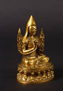A GILT BRONZE FIGURE OF TSONGKHAPA: The figure is seated in vajrasana on double lotus base with his hands in dharmachakra mudra. A pair of lotus flowers trail along his upper arms and support the Sword of Knowledge and the Book of Wisdo