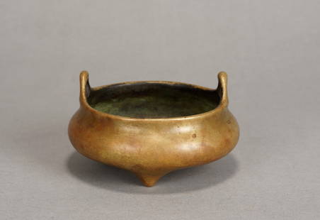 A GILT BRONZE TRIPOD CENSER: The censer is of compressed form with two upright lug handles and rounded tripod feet. The base is cast with a six-character mark within a cartouche. Late Ming Dynasty, Chongzhen period. Height: 2 2/8