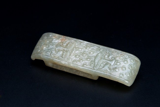 A CHINESE JADE SWORD ORNAMENT: This jade sword ornament was carved with two "Taotie" marks amongst the grain patterns in the style of Han Dynasty. L: 2 7/8 in (7.2 cm)