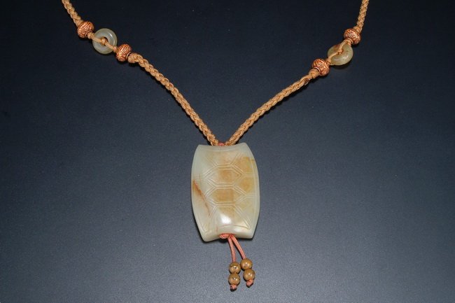 A CHINESE "TURTLE SHELL" JADE ORNAMENT: This jade ornament is in the shape of a turtle shell, the surface is carved with patterns symbolizing the turtles. It signifies the wishful longevity, and natural stone color was well used. L: 1 7/8 i