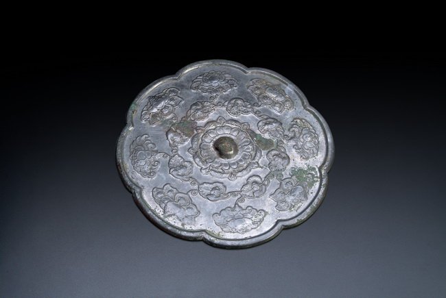 A CHINESE ARCHAIC BRONZE "LOTUS" MIRROR: This circular mirror with foliate edges was well casted with delicate flowery patterns. The raised center knob is of plain circular dome shape. Han Dynasty period. D: 8 1/4 in (21 cm)
