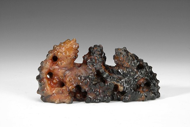 A DUAL COLORED STONE PEN HOLDER: The stone pen holder has three tips with rugged textures all around. The stone is naturally colored with black and brown. L: 6 1/4 in (16cm) H: 3 1/4 in (8cm)