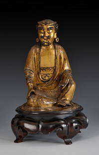 A GILT BRONZE ARHAT STATUE: The gilt bronze Arhat statue is in a sitting posture, dressed in robe, with serene expression, and eyes closed. It is completed with a hardwood base. Qing Dynasty period. Dimensions: H: 7 3/4 in (19.5